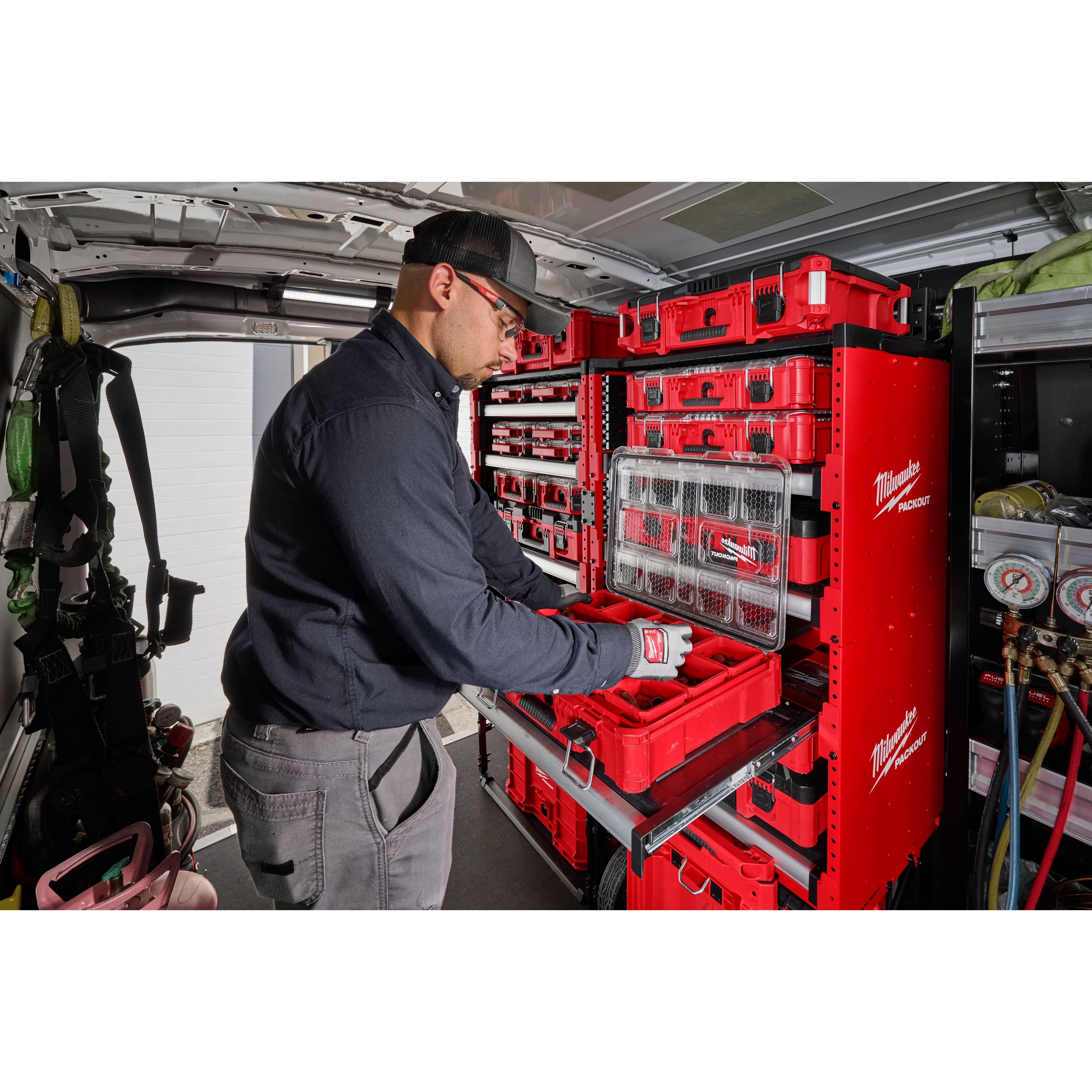 A worker organizes tools using the PACKOUT™ Rack Kit installed in a van. The red storage system includes multiple shelves and compartments, holding various Milwaukee toolboxes and organizers, ensuring efficient storage and easy access to tools.