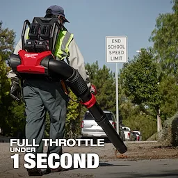 A person uses the M18 FUEL™ Dual Battery Backpack Blower on a sidewalk. The blower is red and black with two batteries. The background shows trees and an "End School Speed Limit" sign. Text reads, "FULL THROTTLE UNDER 1 SECOND."