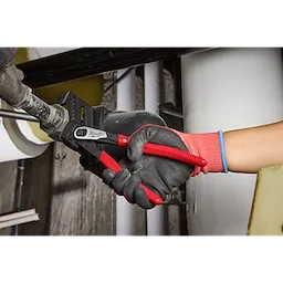 A person wearing a black and red glove uses 12" Pliers Wrench with red handles to adjust a pipe in an industrial setting.