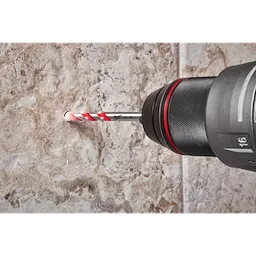 A 1/4" Hard Tile and Glass Bit is being used in a drill to create a hole in a beige, marble-like tile surface. The bit features a red and white spiral design for effective drilling in hard tiles and glass materials. Dust is visible around the drilled hole.