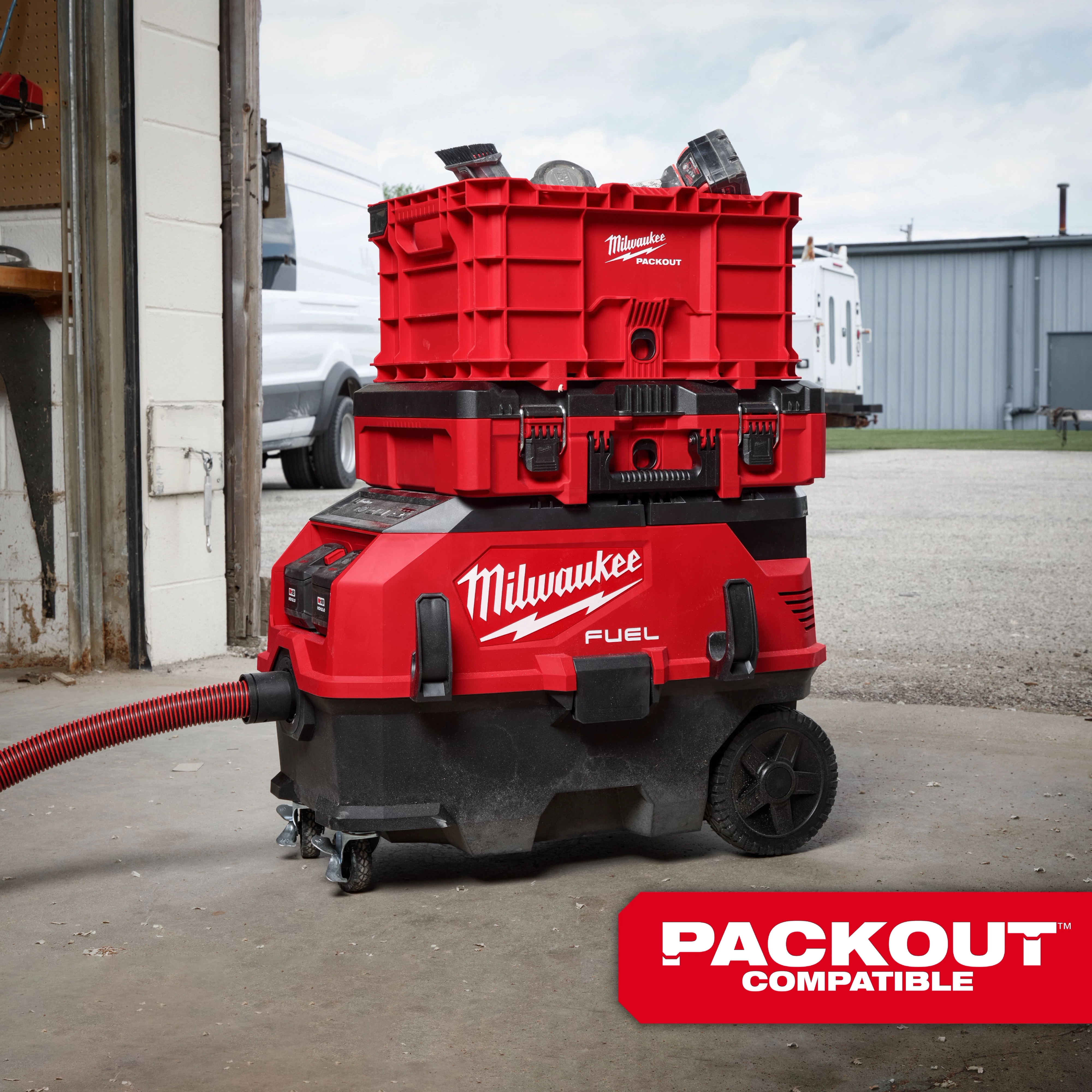 The image shows the M18 FUEL™ 9 Gallon Dual Battery Dust Extractor with PACKOUT™ Compatibility and VACLINK™. The red and black dust extractor has wheels, a hose, and stacked PACKOUT™ storage units on top, and is branded with "Milwaukee FUEL." A "PACKOUT Compatible" label is visible.