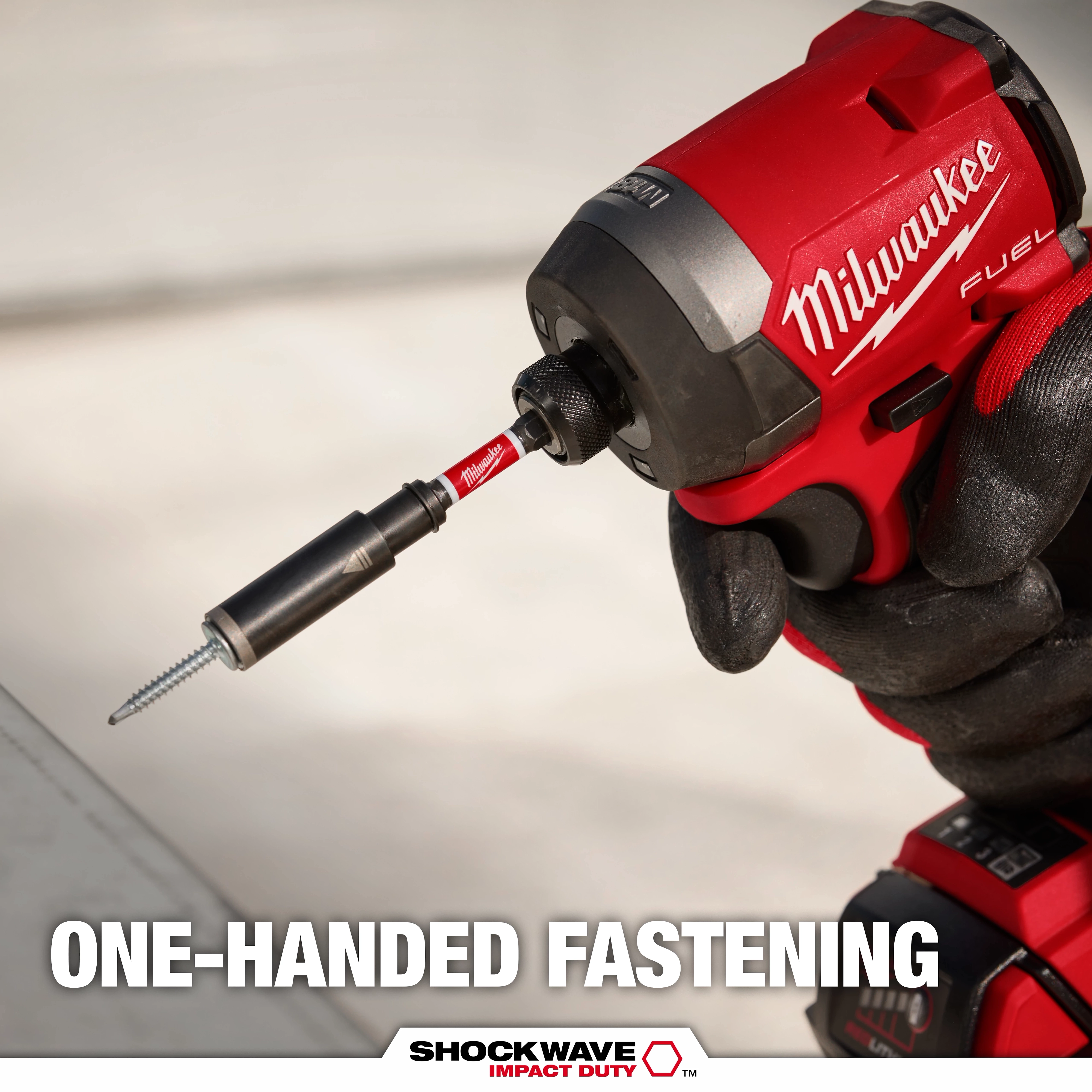 A close-up of a gloved hand using a Milwaukee Fuel impact driver with a Shockwave Impact Duty bit to fasten a screw. The text at the bottom reads “ONE-HANDED FASTENING.” The advertisement highlights the product's ease of use with one hand.
