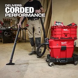 A person uses the M18 FUEL™ NEXUS™ 6 Gallon Wet/Dry Vacuum w/ PACKOUT™ Compatibility in a workshop. The red vacuum is connected to PACKOUT™ storage boxes and features a hose and cleaning attachment. Text on the image reads "Delivers Corded Performance."