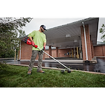 Person using a string trimmer to cut grass near a building with a covered driveway.