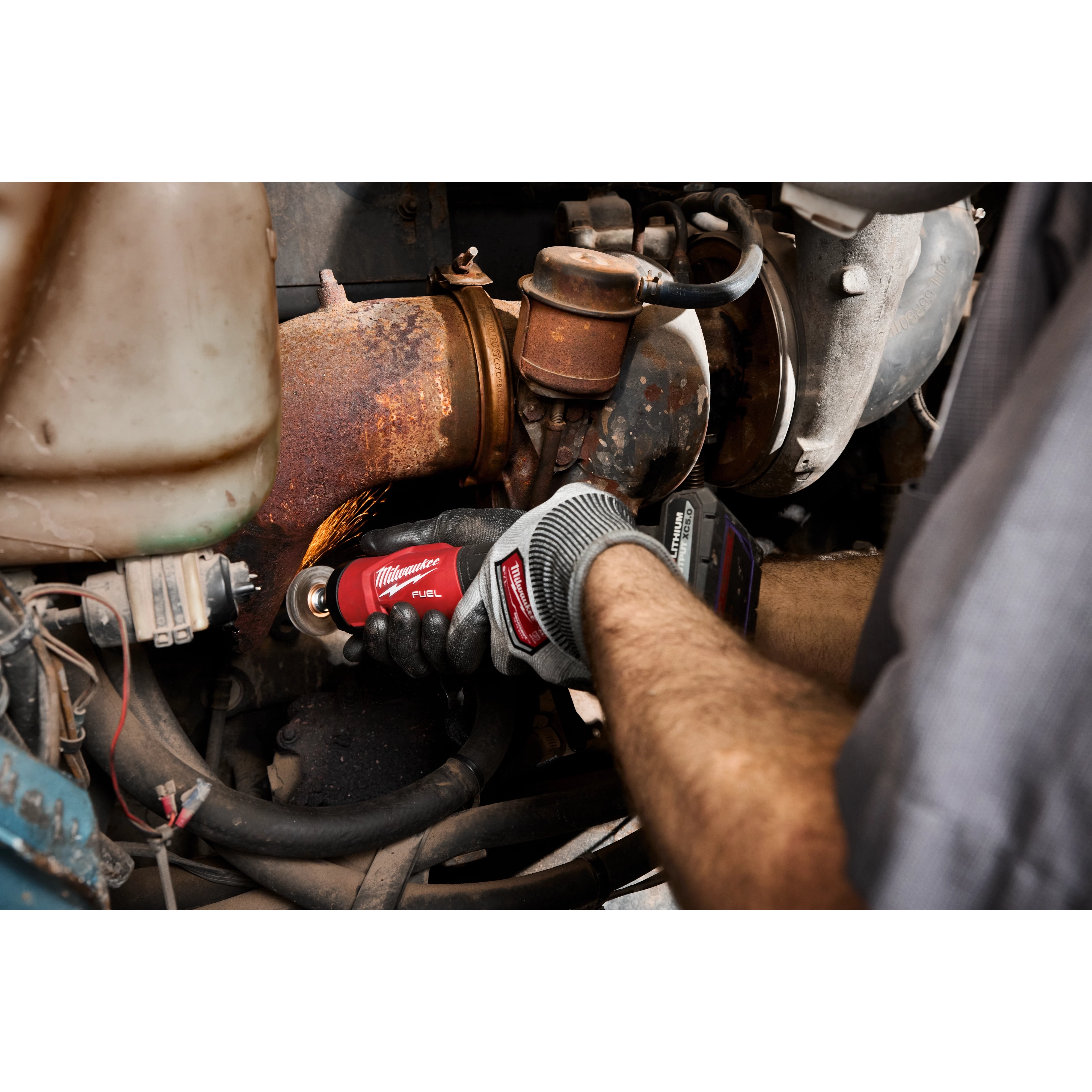 Gloved hands use an M12 FUEL 1/4" Straight Die Grinder on a rusted engine component.