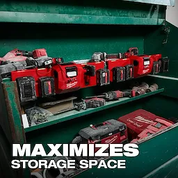 The M18™ and M12™ Gangbox Rapid Charger is mounted in a green storage cabinet, charging multiple Milwaukee batteries. Various tools and accessories are stored on adjacent shelves. The text "MAXIMIZES STORAGE SPACE" is displayed prominently on the image.