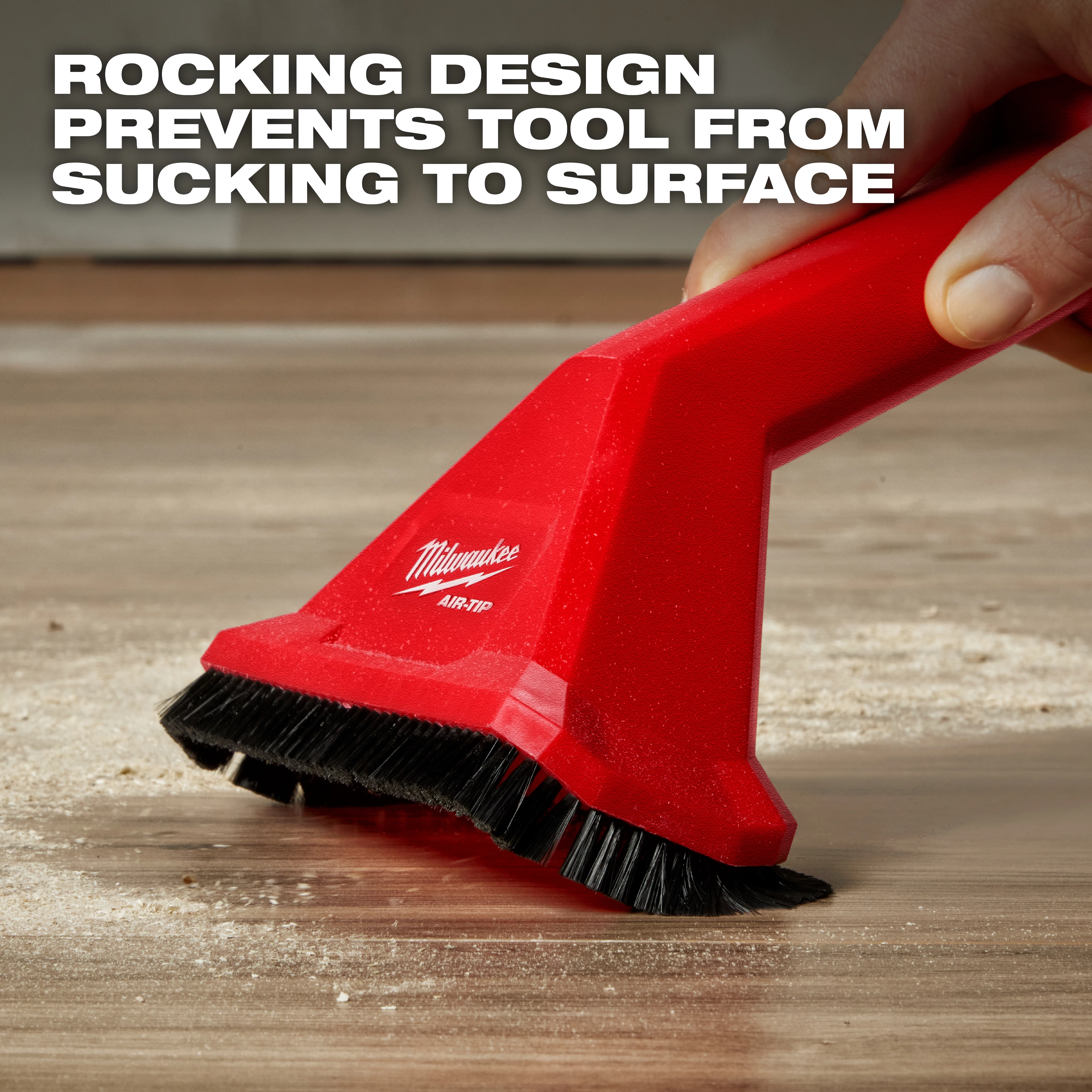 A person uses the AIR-TIP™ Rocking Utility Nozzle with Brushes on a surface with debris. The red nozzle has black bristles and displays the Milwaukee logo. Text above reads: "ROCKING DESIGN PREVENTS TOOL FROM SUCKING TO SURFACE."