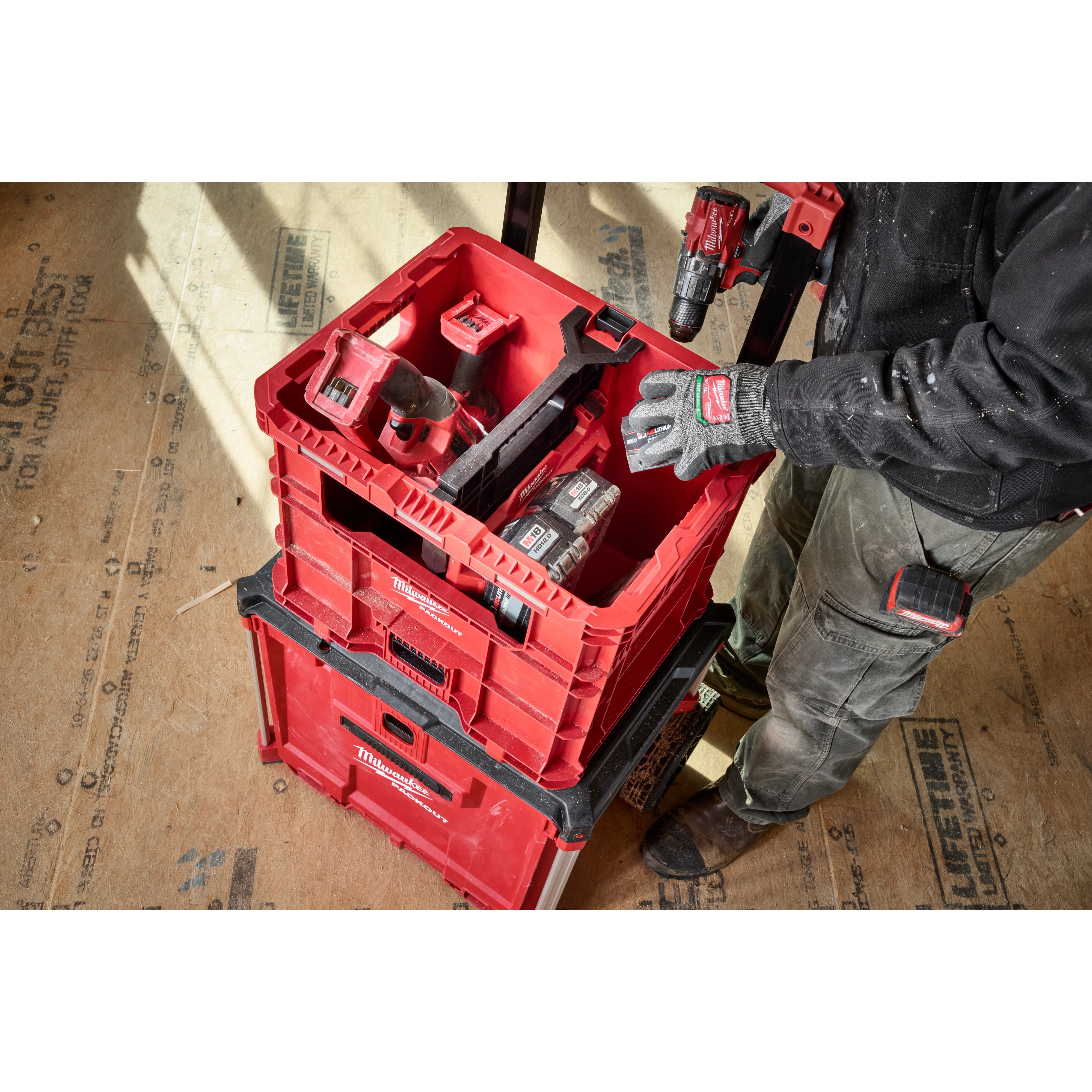 Person using a Divider for PACKOUT XL Crate to organize red tool containers on a construction site.