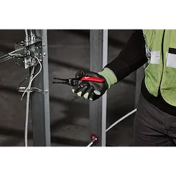 A person in a safety vest and gloves holds a 12/2 & 14/2 NM Dipped Grip Wire Stripper & Cutter. The tool has a black and red handle and is shown in a construction environment with exposed wiring.