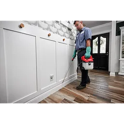 Man using the M12 Handheld Sprayer to spray along wall trim indoors for pest treatment