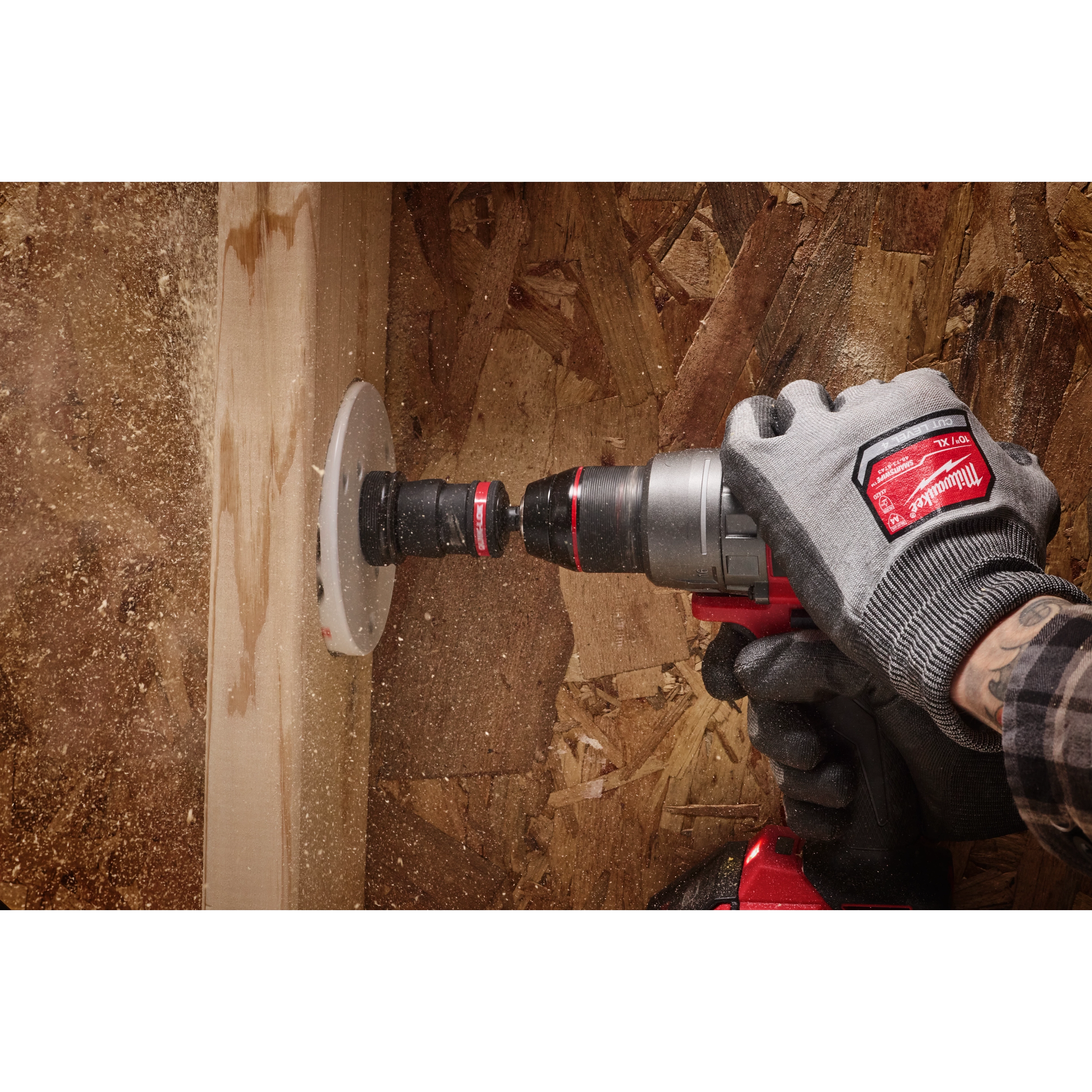 A person wearing gloves uses a power drill equipped with a 3/8" QUIK-LOK™ Arbor Set to drill a hole in a wooden surface. Wood dust is visible around the drill bit, and the background consists of unfinished wooden boards.