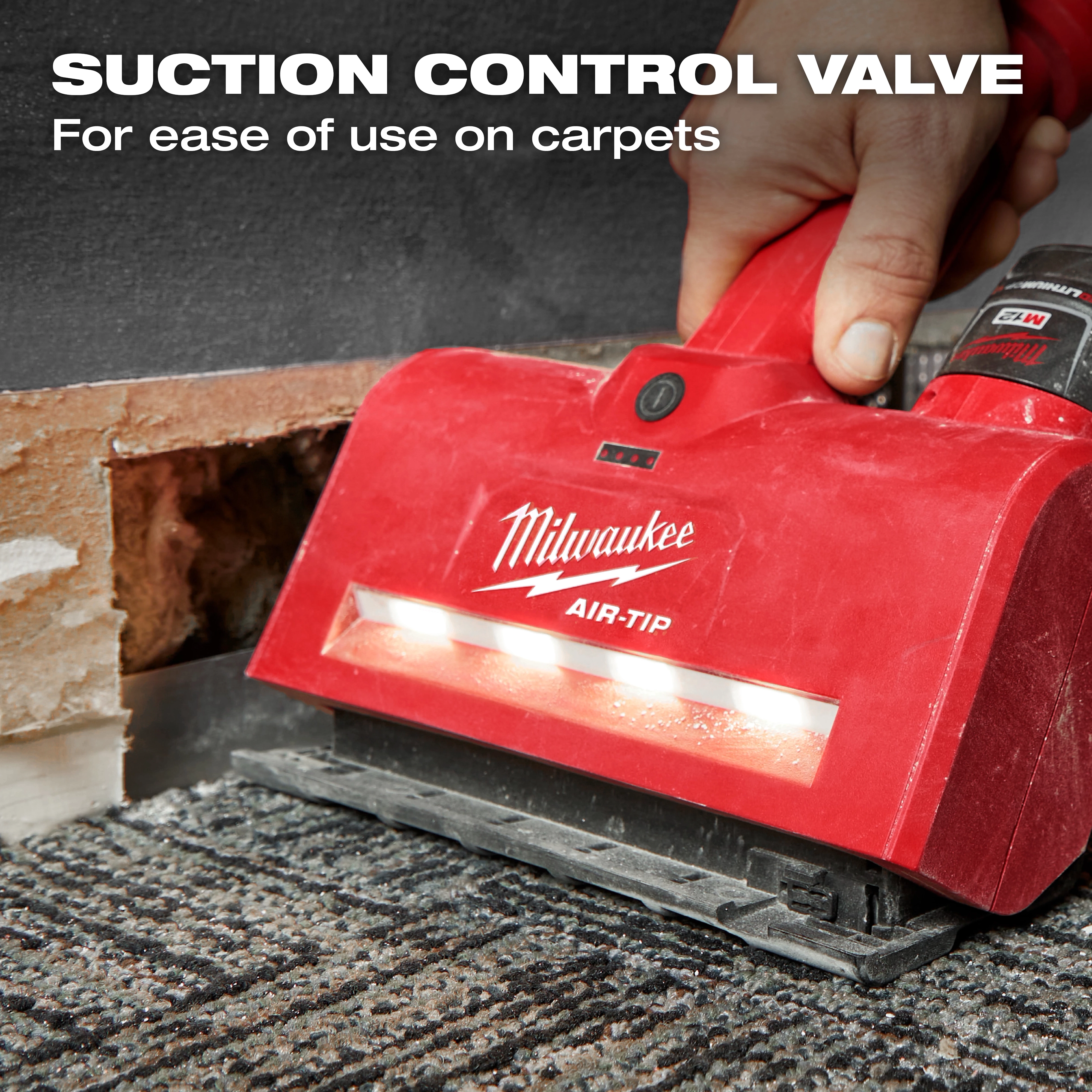 A hand using the red M12™ AIR-TIP™ Utility Nozzle on a carpet. The nozzle has a suction control valve for ease of use on carpets. A partially exposed wall is visible in the background. Text on the image highlights the suction control valve feature.