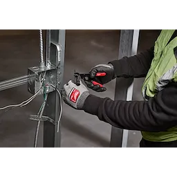 A person wearing gloves uses a 10-24 AWG Adjustable Compact Wire Stripper & Cutter to strip wires connected to a metal frame.