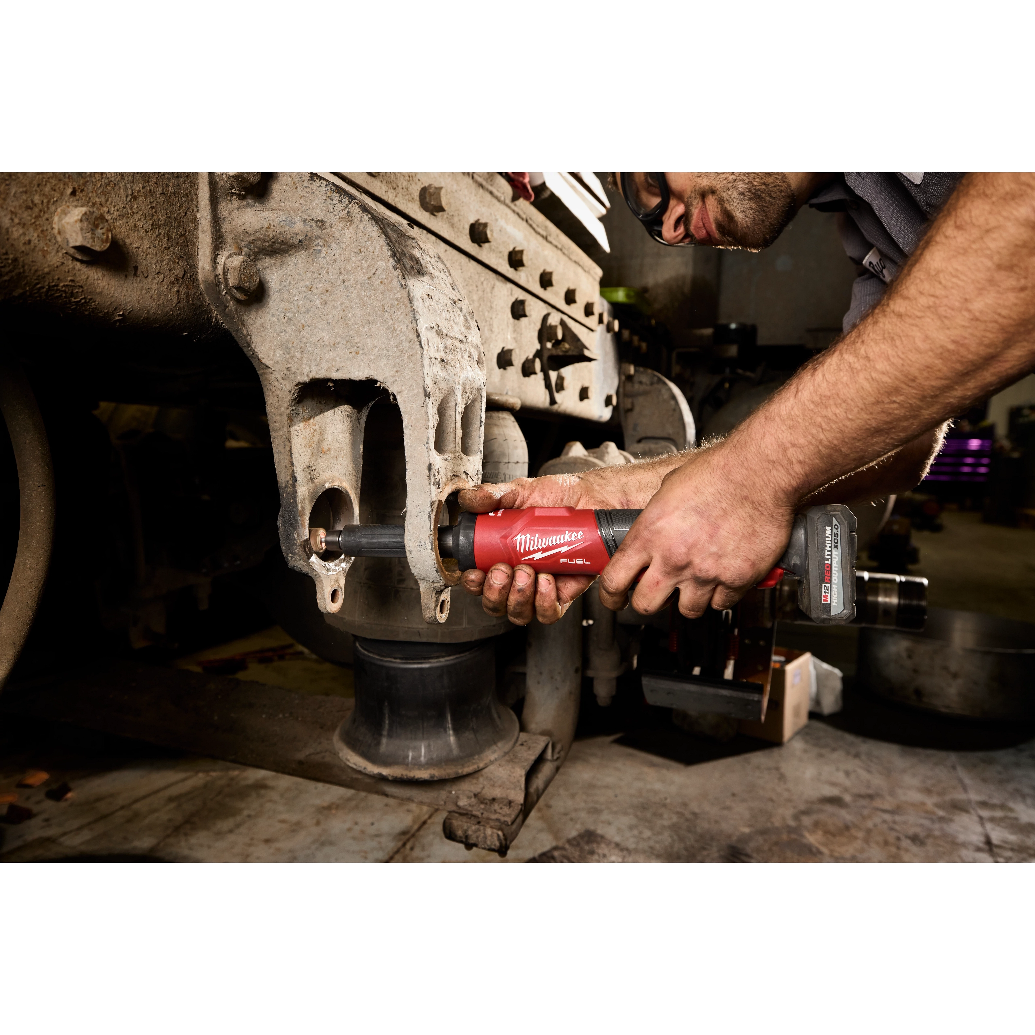 Worker using an M12 FUEL 1/4" Extended Die Grinder on a large metal machine part.