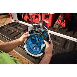 Hands holding a white hard hat with the BOLT REDLITHIUM USB Cooling Fan attached inside, against a background of red toolboxes and road case.