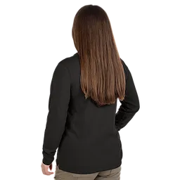 A woman with long, straight brown hair is seen from behind. She is wearing a black long-sleeve shirt and beige pants. She stands with one hand on her hip.