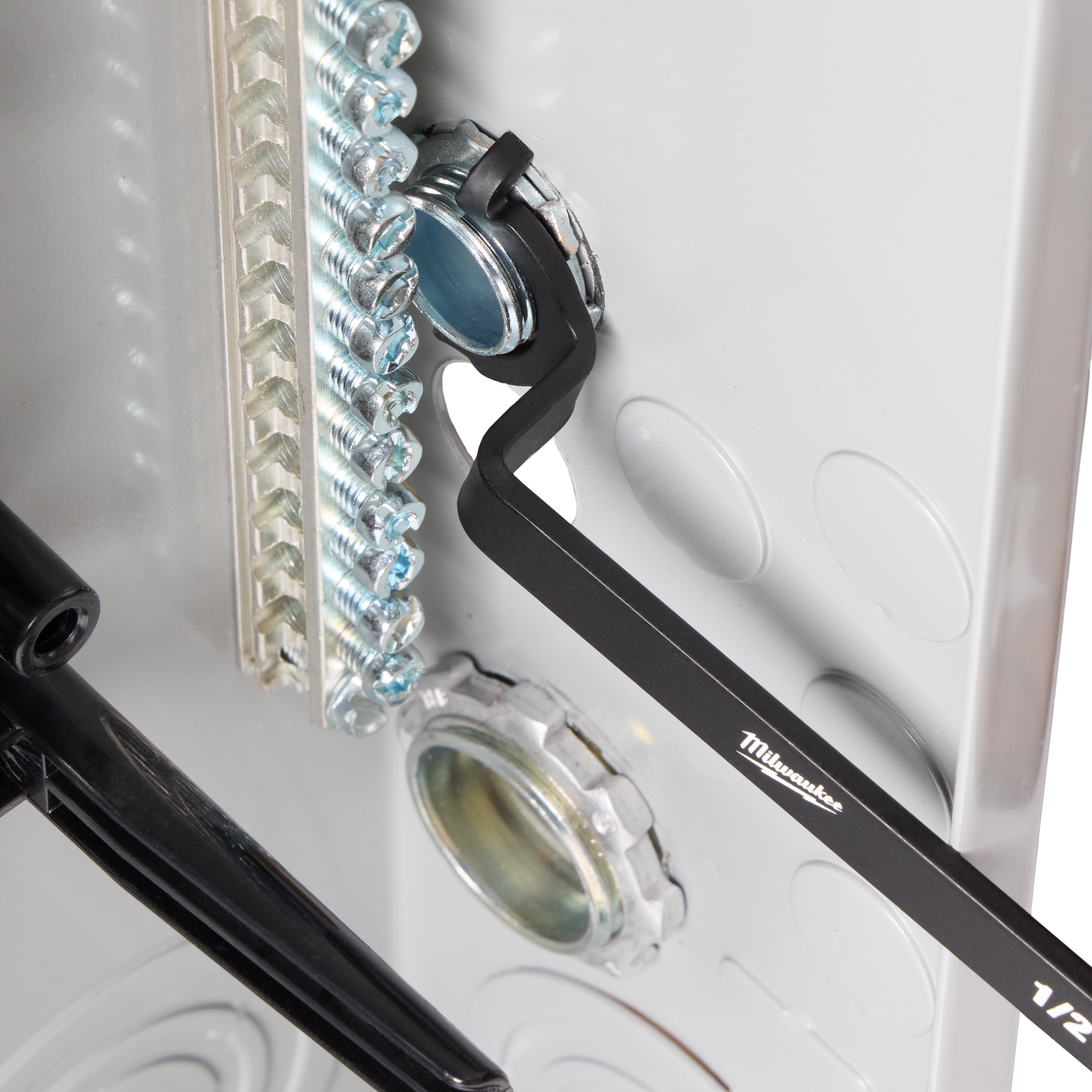 The 3 PC Locknut Wrench Set by Milwaukee is shown in use, tightening a locknut inside an electrical panel. The wrenches have a black finish and are designed for efficient fastening in tight spaces.