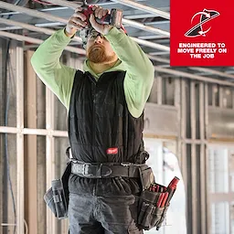 A person wearing the FREEFLEX™ Lightweight Insulated Vest is working on a construction site. The vest is black and designed for mobility, with multiple tool belts and pouches attached. The background includes metal frame structures under construction. A slogan reads "ENGINEERED TO MOVE FREELY ON THE JOB."