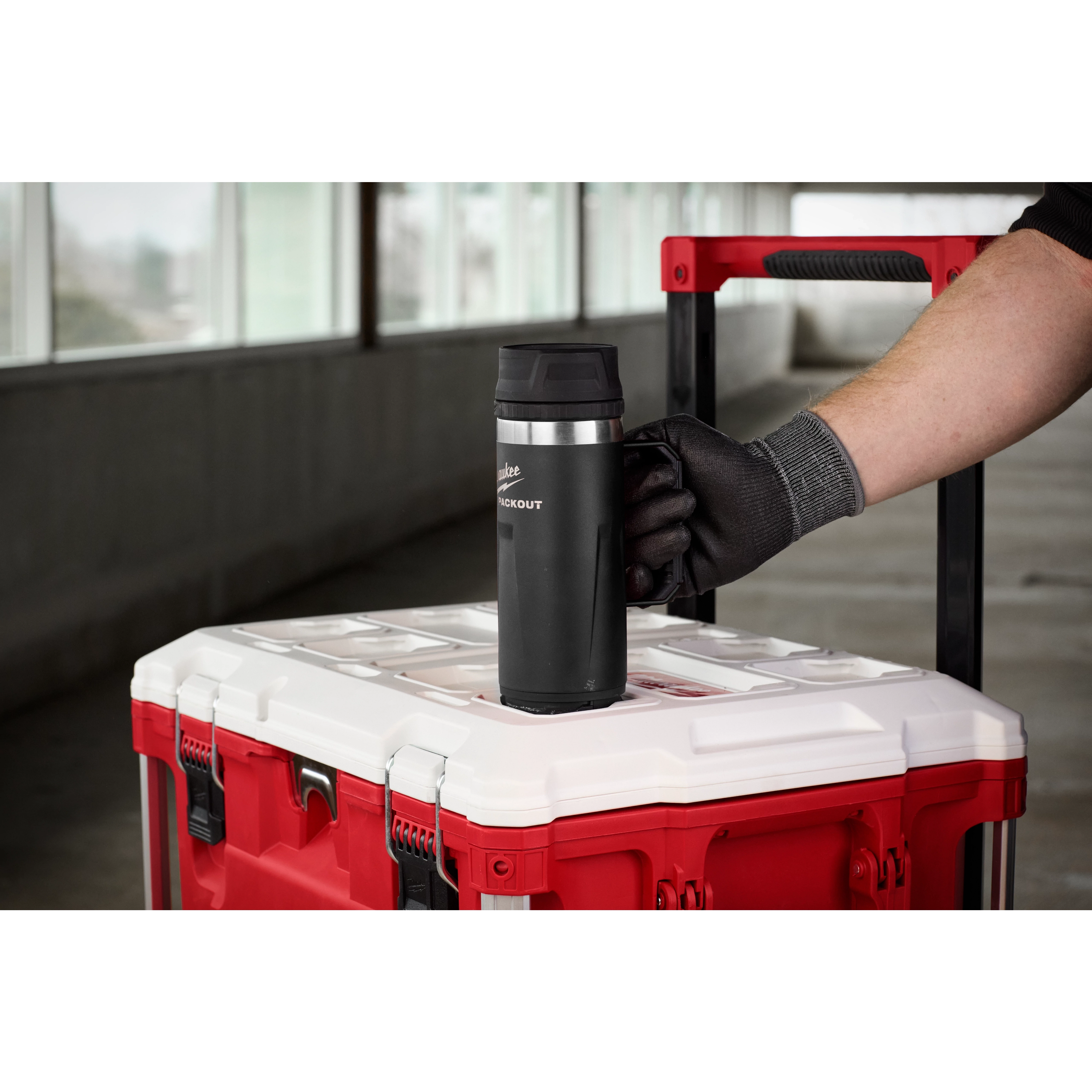 A person wearing a black glove places the PACKOUT 18oz Insulated Mug with Sip Lid on top of a red and white tool box.