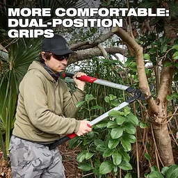 A person wearing a green hoodie and camouflage pants uses a 2" Lopper to cut a tree branch. The text "More Comfortable: Dual-Position Grips" is displayed at the top of the image.