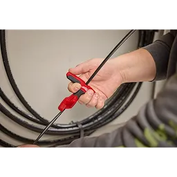 A person is holding a Fiber Optic Drop Cable Slitter, a tool with a red handle, to cut through a black fiber optic cable, with coiled cables visible in the background.