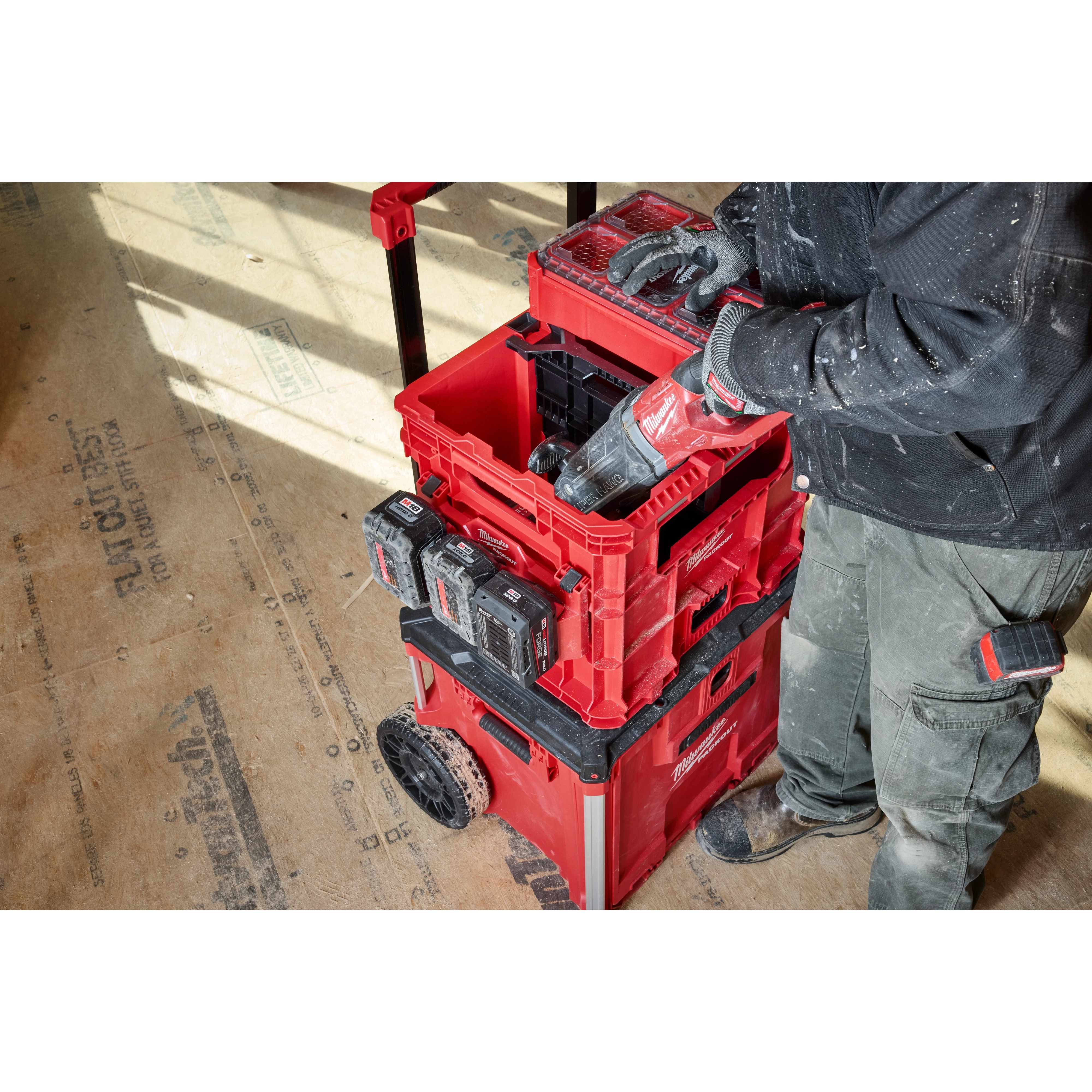 Worker using a power tool with Divider for PACKOUT XL Crate integrated in a red modular toolbox system with crates on a job site.