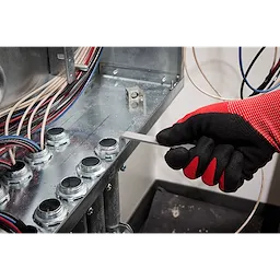 A gloved hand uses a wrench from the 3 PC Locknut Wrench Set to tighten a locknut inside an electrical panel. Multiple wires and locknuts are visible inside the panel, and the hand is wearing black and red gloves for protection. The wrenches are designed for electrical work.