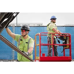Construction workers wearing Wrap-Around Safety Glasses with red Mirrored Anti-Scratch Lenses operate a scissor lift. They are on a building site and wear protective gear, including helmets and high-visibility vests, emphasizing safety protocols.
