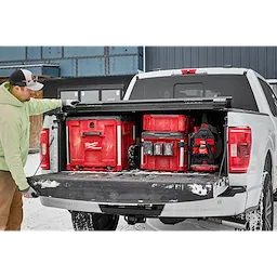 A person is loading a PACKOUT™ Rolling Drawer Tool Box and other PACKOUT™ storage boxes into the bed of a white truck on a snowy day.
