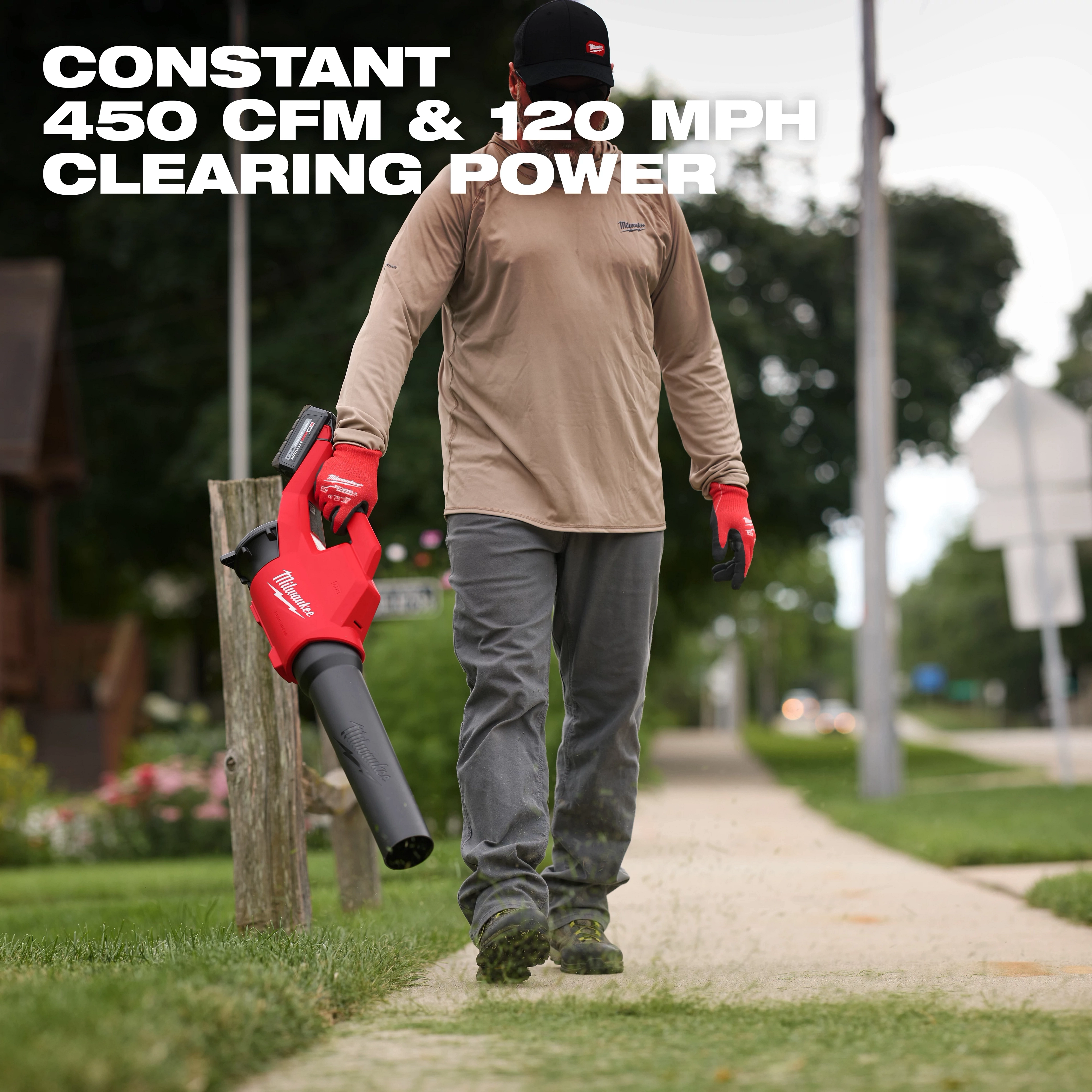 A person uses the Milwaukee M18 Brushless Blower to clear a sidewalk. The blower delivers 450 CFM and 120 MPH clearing power.