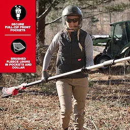 A person stands outside holding a power tool, wearing the Women's FREEFLEX™ Lightweight Insulated Vest in Black. The vest features secure full-zip front pockets and brushed fleece lining in pockets and collar. A tractor is visible in the background.