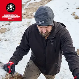Person outdoors in snow wearing a Milwaukee Sherpa-Lined Beanie and work jacket, climbing a snowy slope.