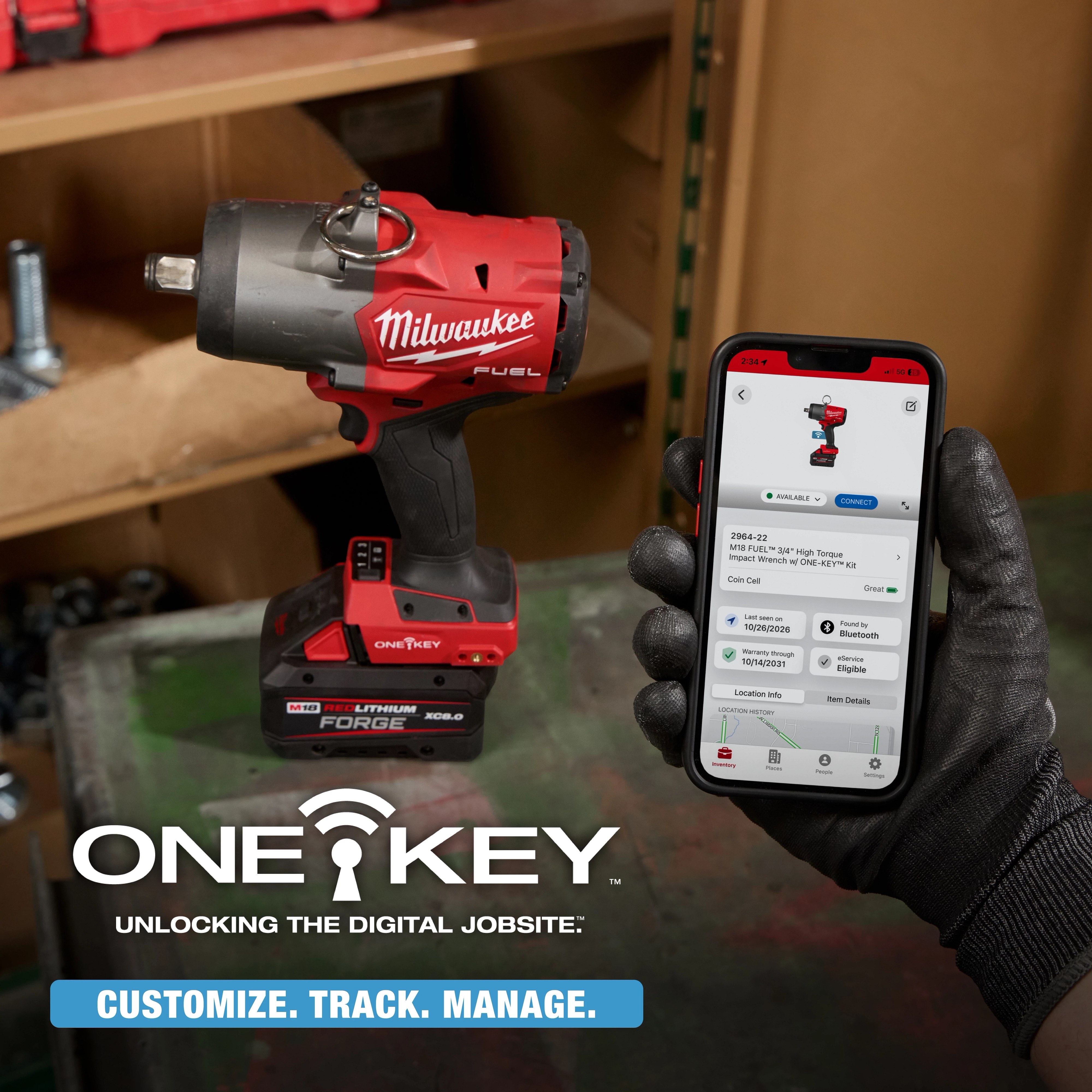 Gloved hand holds a phone showing M18 FUEL 3/4" High Torque Impact Wrench w/ ONE-KEY Kit beside the wrench on a workbench.