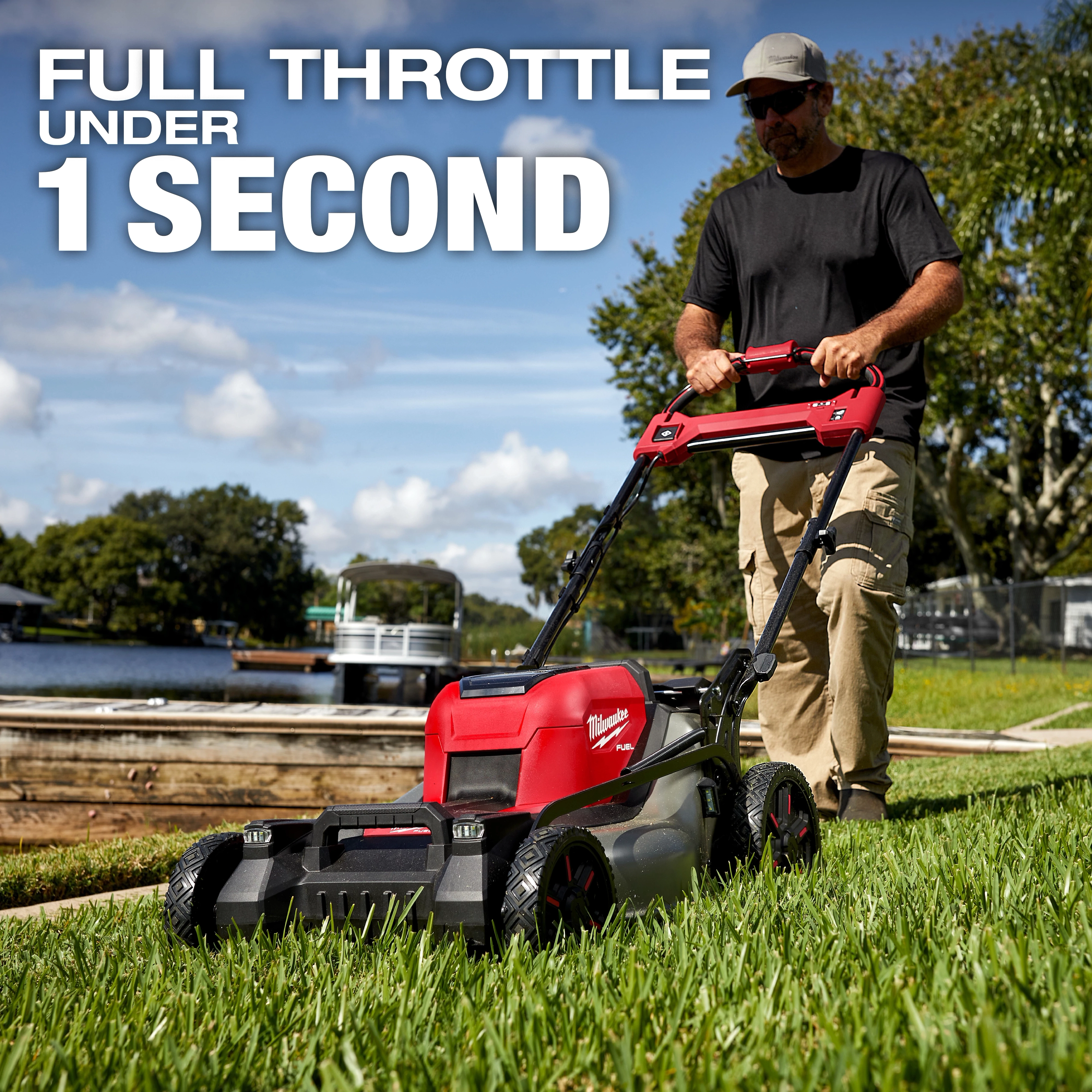 A person operates the M18 FUEL™ 21" Self-Propelled Dual Battery Mower on grass near a waterfront. Text on the image reads, "Full Throttle Under 1 Second." Trees and a dock are visible in the background.
