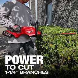 A person is using the M18 FUEL™ 24" and 30" Hedge Trimmer to trim a hedge. The text on the image states, "POWER TO CUT 1-1/4" BRANCHES." The hedge trimmer is red with black handles and labeled with the Milwaukee brand.