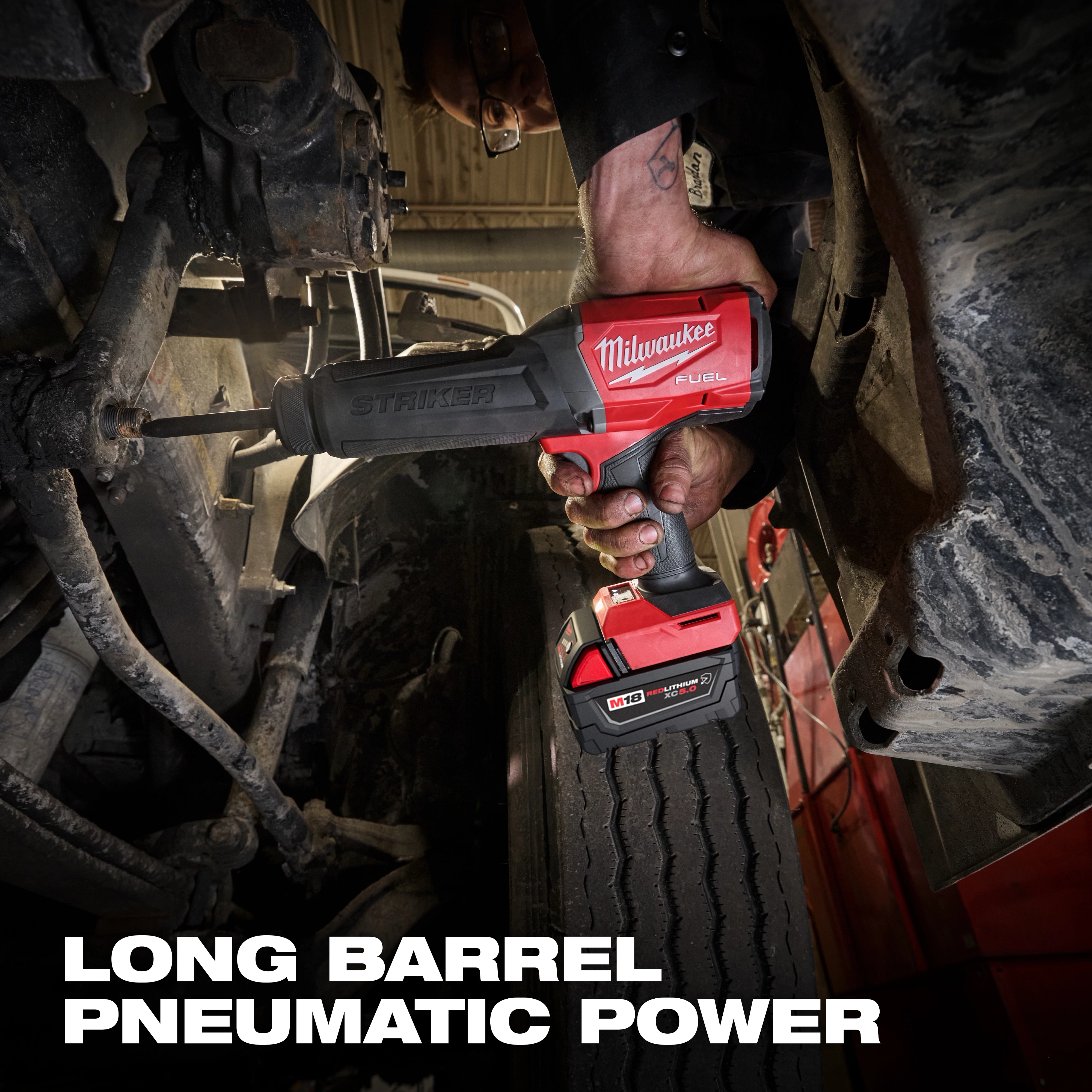 Hand holding an M18 FUEL STRIKER Hammer Chisel between vehicle parts above a large tire.
