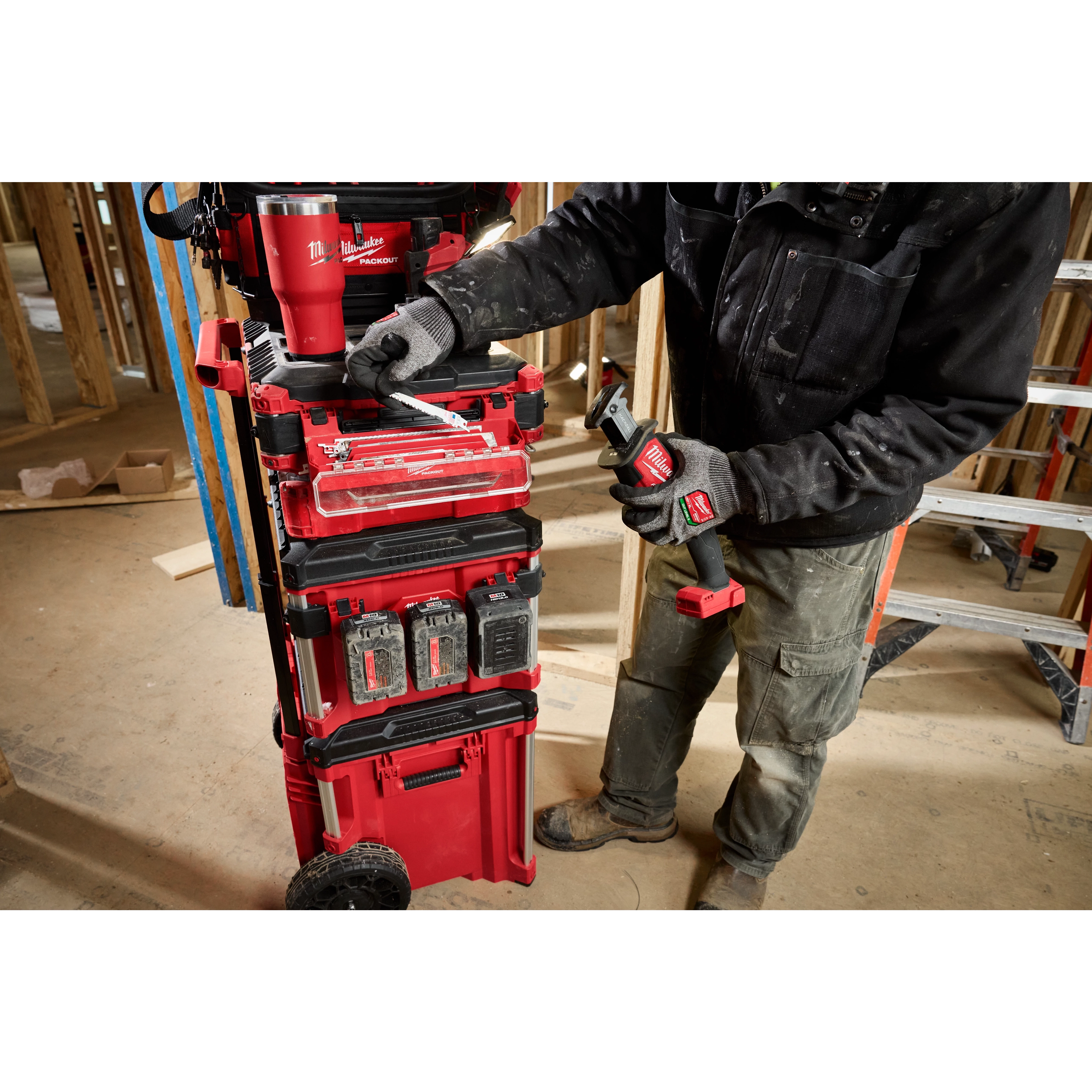 A worker adjusts a PACKOUT Tool Box Accessory Case Attachment on a red rolling tool chest at a construction site.