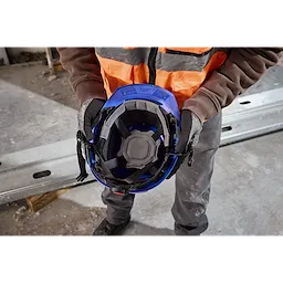 Worker holds BOLT 4PT Blue Front Brim Non-Vented Safety Helmet – Type 2, Class E, showing the interior suspension system and padding.