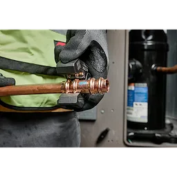 The 1/4" - 7/8" Streamline® ACR Pivoting Press Ring Kit is shown being used with the M18™ FORCE LOGIC™ press tool on a copper pipe. The image depicts a close-up of hands wearing gloves, pressing a fitting onto the pipe in an industrial environment.