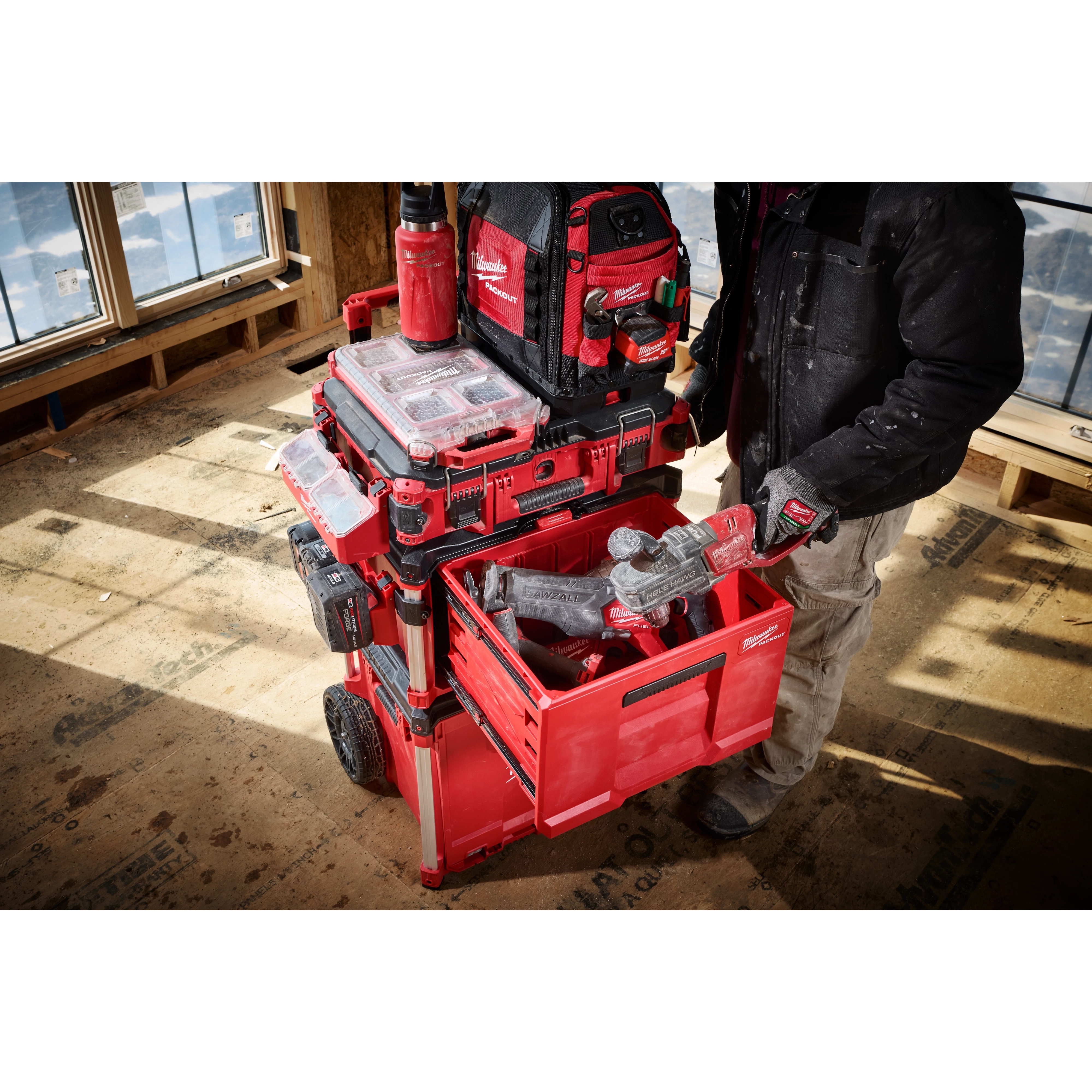 Milwaukee Packout rolling toolbox stacked with red tool cases and bags on a construction floor.