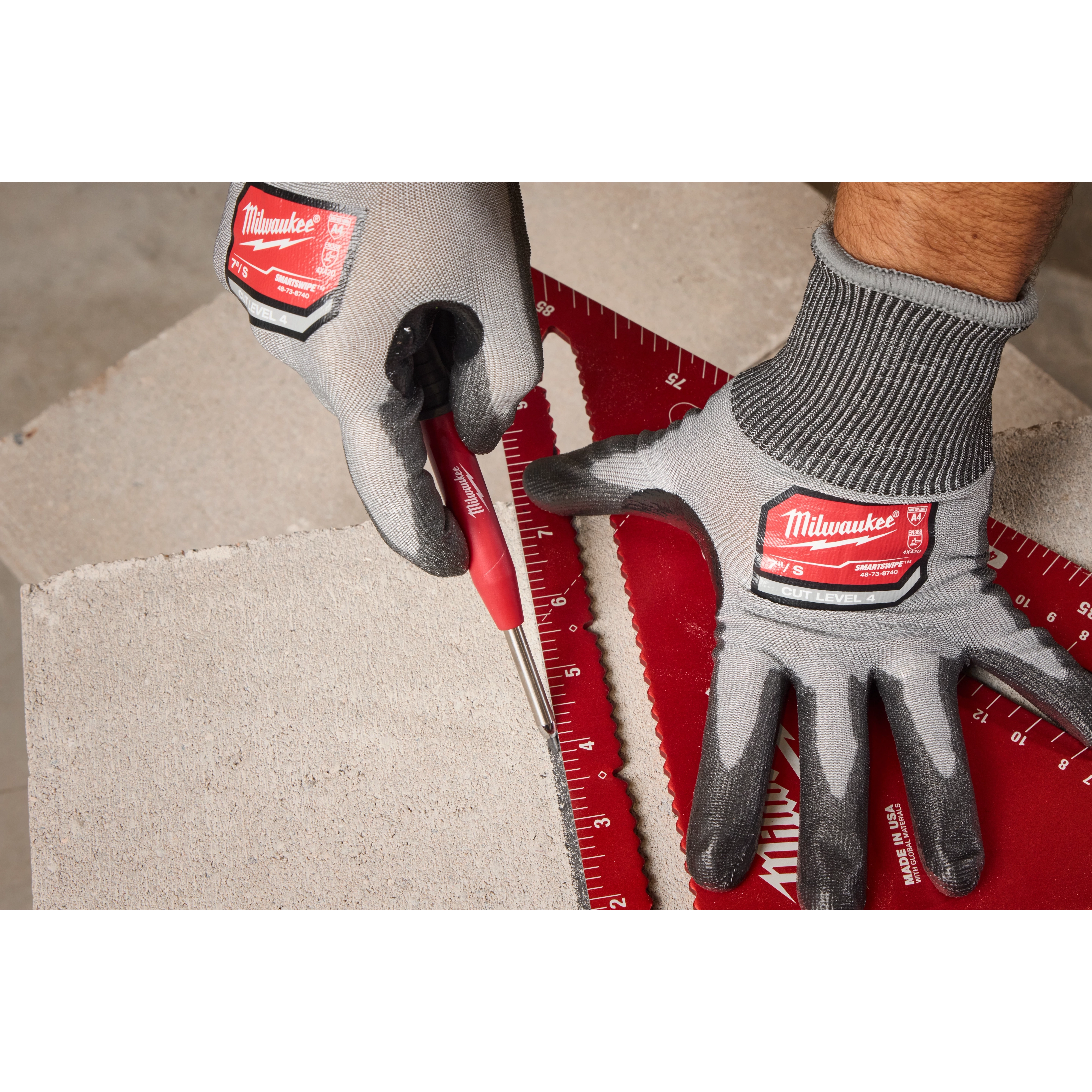 A gloved hand uses a Milwaukee Mechanical Pencil to draw a line along a red ruler on a concrete block. The setting suggests a construction or workshop environment. The Mechanical Pencil is held in the right hand for precise marking.