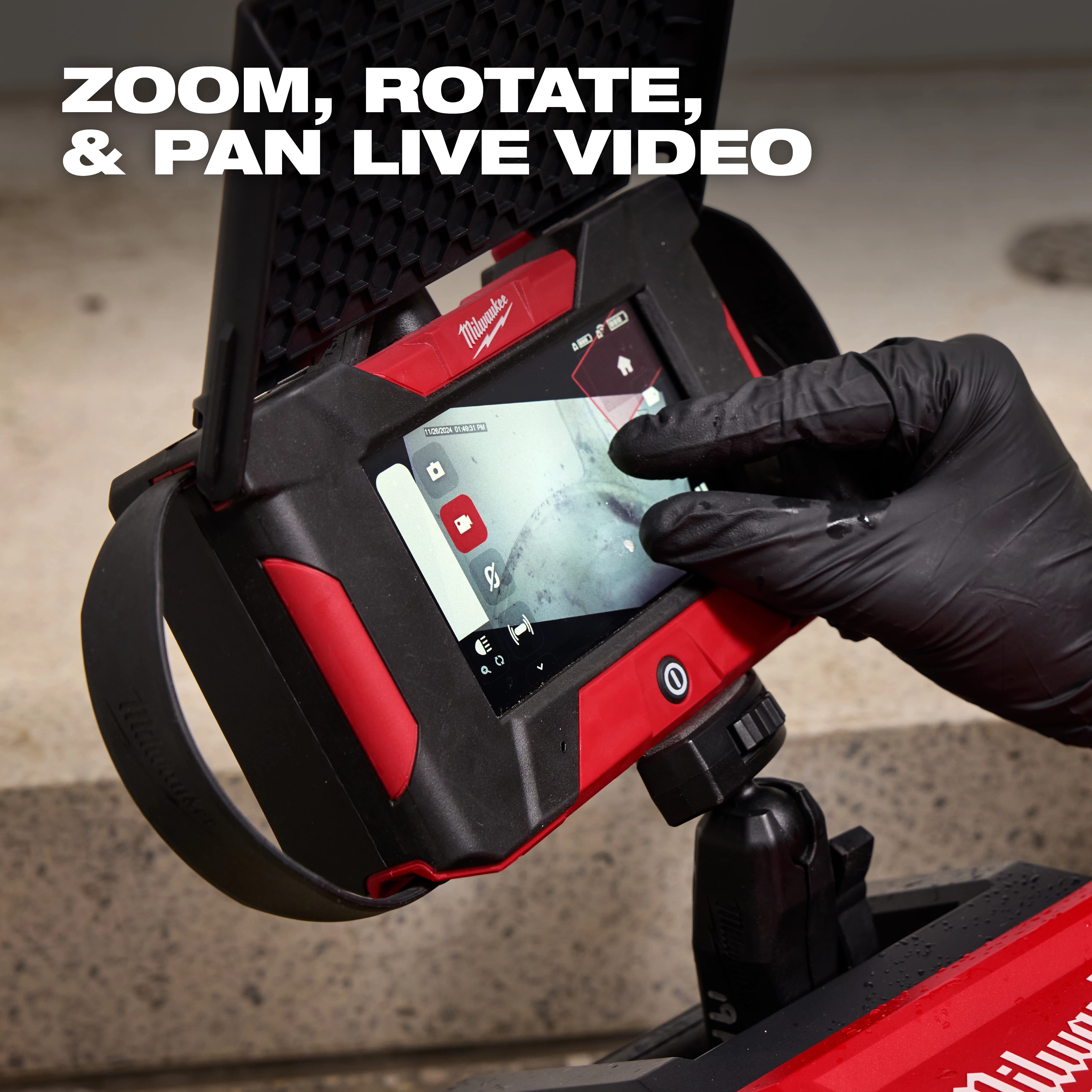 A close-up of a gloved hand operating a Milwaukee inspection camera. The screen shows a live video feed, and text at the top reads "ZOOM, ROTATE, & PAN LIVE VIDEO."