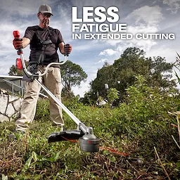 A person operates a grass trimmer in a garden, surrounded by overgrown vegetation. The text in the image reads, "LESS FATIGUE IN EXTENDED CUTTING." The person is wearing a harness and holding the trimmer with both hands. A house and trees are visible in the background.