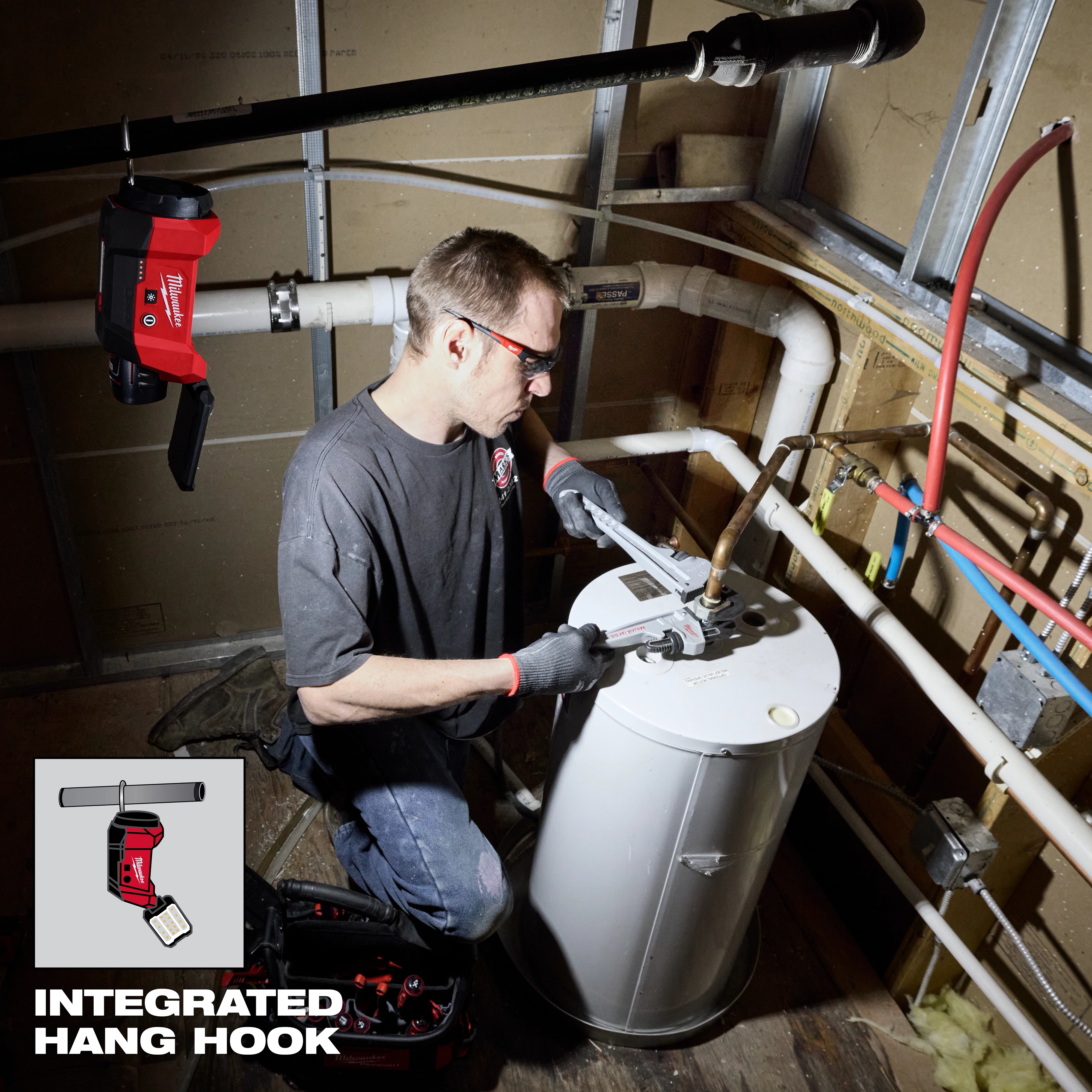 A worker uses a Milwaukee M12 FUEL Pipe Threader Kit to service a pipe system. The image showcases an integrated hang hook feature, allowing the tool to be suspended from a pipe. The equipment and accessories are neatly organized nearby.