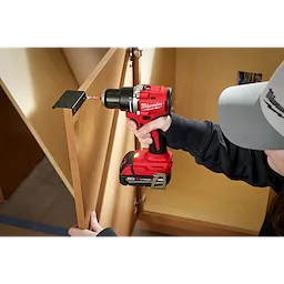 A person uses the M18 Compact Brushless 1/2" Drill/Driver to install a hinge on a wooden cabinet door indoors.