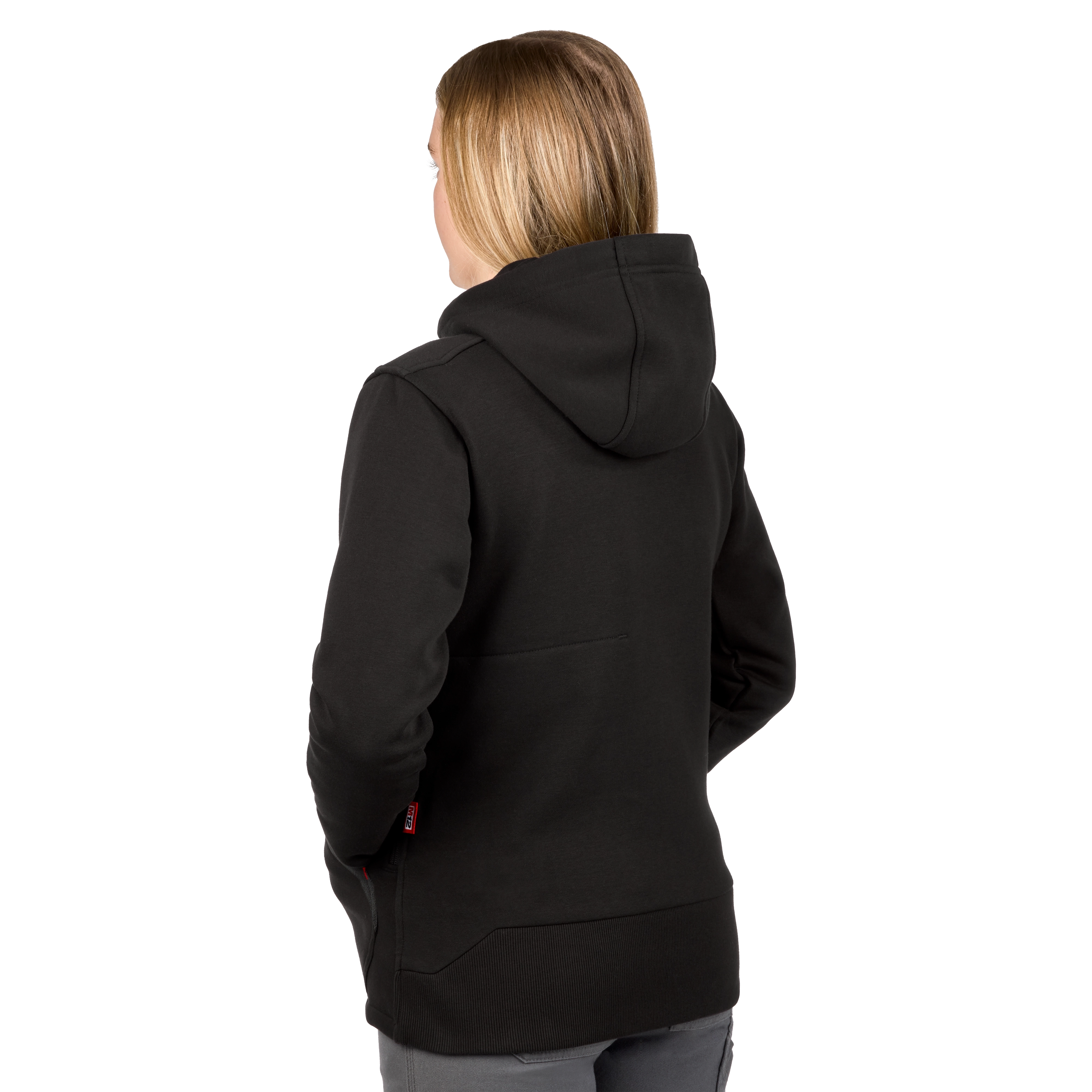 The image shows a woman from the back wearing an M12™ Women's Heated Hoodie in black. She has shoulder-length blonde hair and the hoodie features a hood and long sleeves.