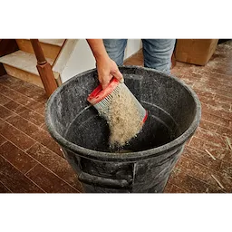 Person emptying the MILWAUKEE Large Wet/Dry Vacuum High Efficiency Filter filled with dust into a black trash bin.