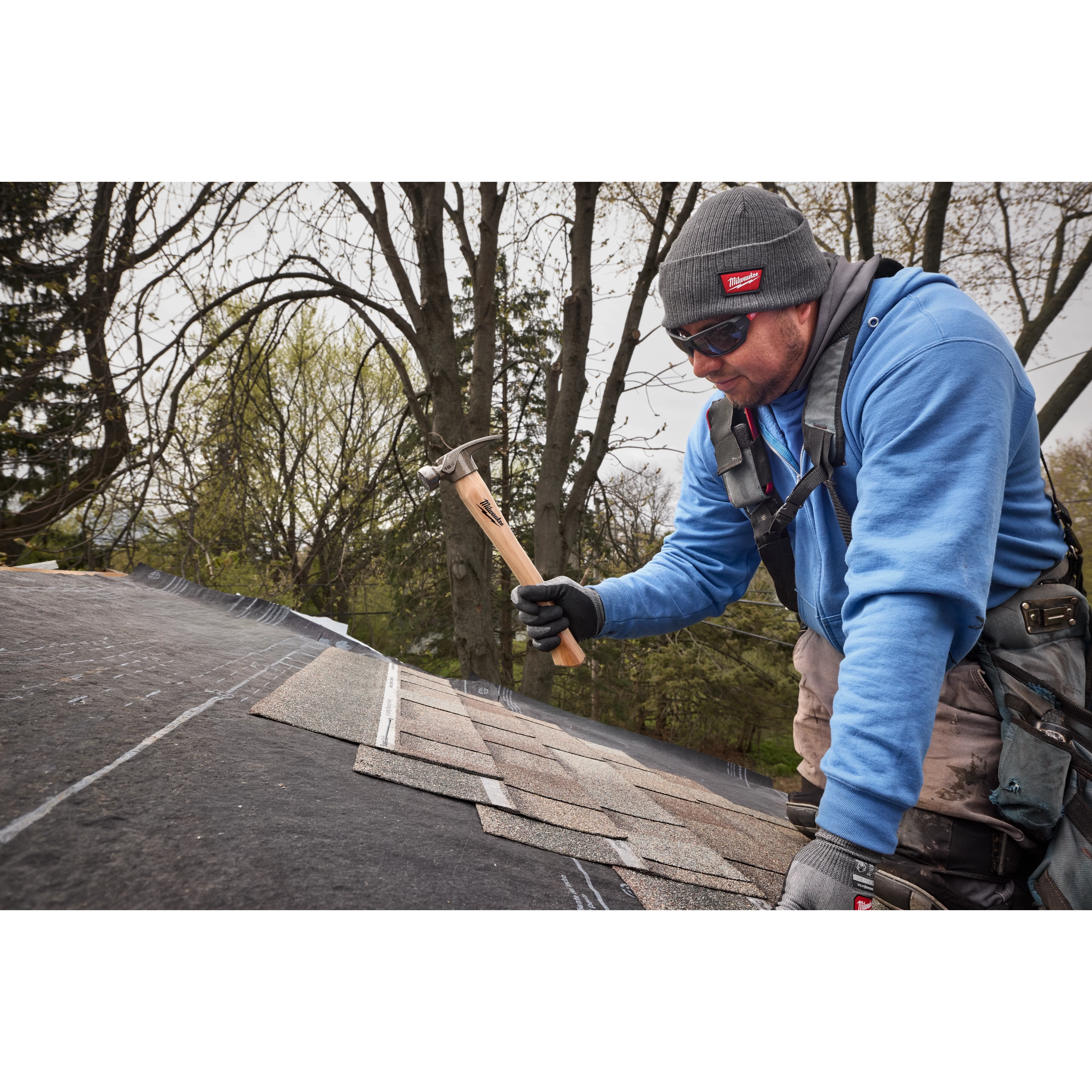 Worker on a roof holding a 16oz Smooth Face Hickory Handle Hammer over shingles.