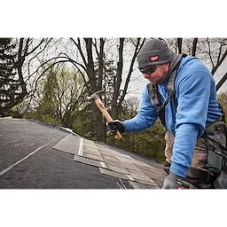 Worker on a roof holding a 16oz Smooth Face Hickory Handle Hammer over shingles.