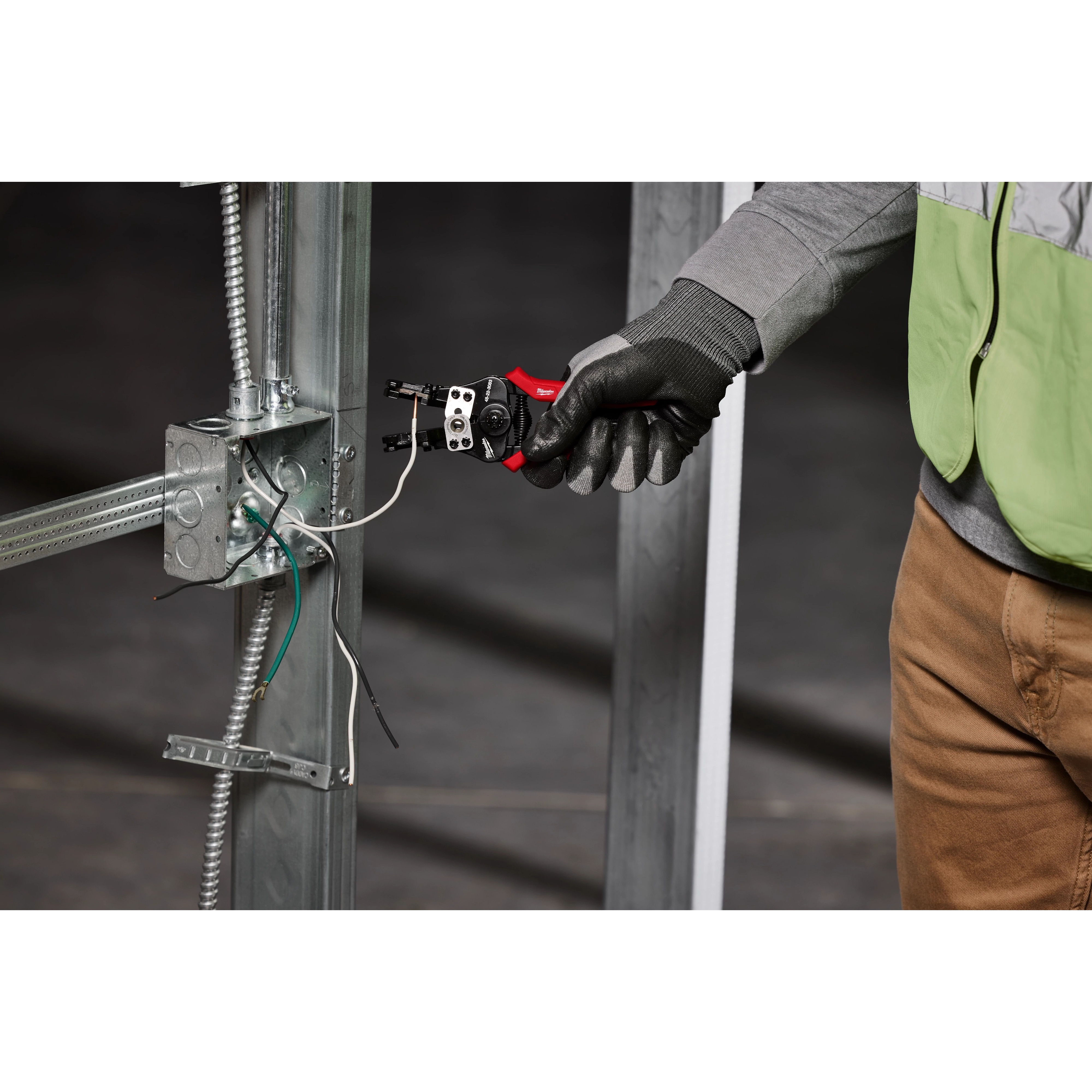 A person wearing gloves uses an Automatic Wire Stripper & Cutter to strip wires connected to a metal electrical box framework.